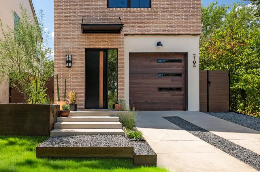 A modern brick facade highlights the entryway and sleek matching wood garage doors. A modern brick facade highlights the entryway and sleek matching wood garage doors.