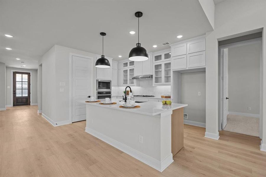Modern kitchen featuring an island with two pendant lights, white cabinetry, integrated appliances, and a gas range Modern kitchen featuring an island with two pendant lights, white cabinetry, integrated appliances, and a gas range