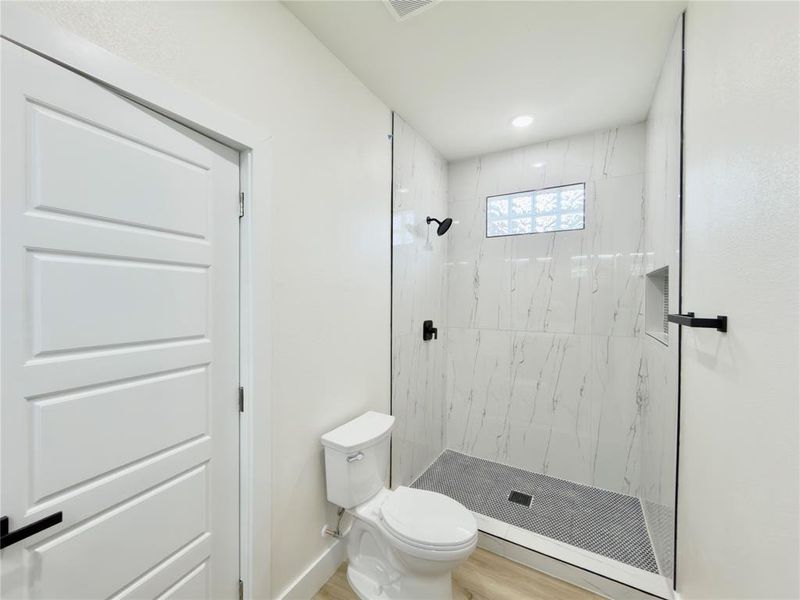 Walk-in shower featuring marble-look tile, glass block window, matte black fixtures, and a recessed niche