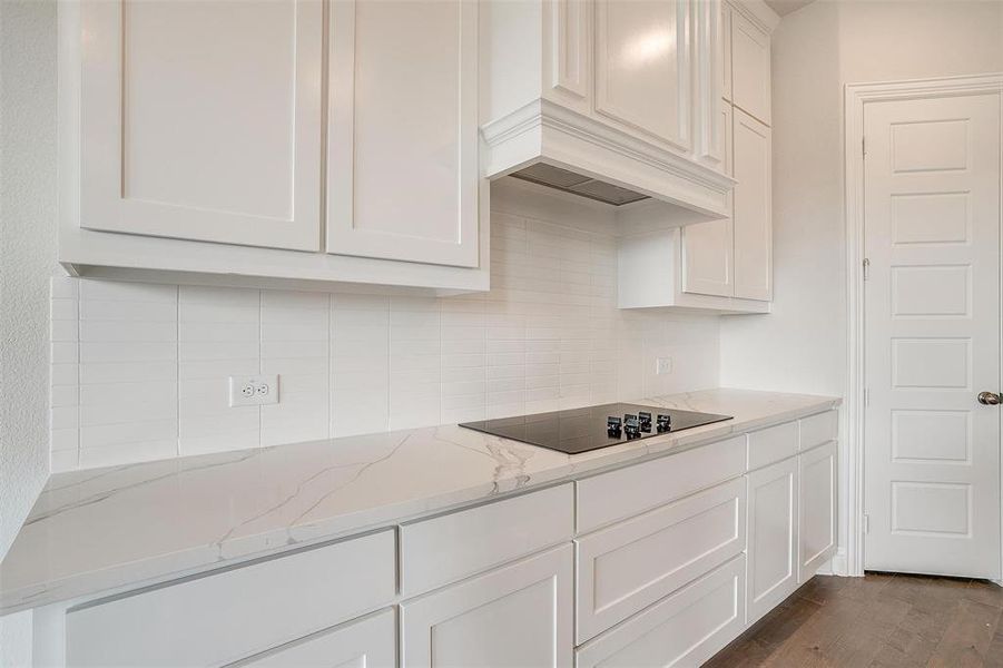 Kitchen featuring black electric stovetop, dark hardwood / wood-style floors, light stone countertops, white cabinetry, and tasteful backsplash