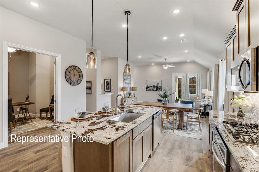 Kitchen featuring light hardwood / wood-style floors, vaulted ceiling, stainless steel appliances, decorative light fixtures, and a center island with sink