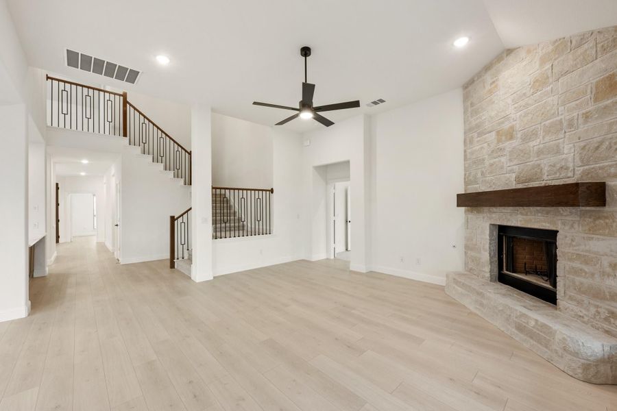 Open living room with stone fireplace, ceiling fan, hardwood floors, and staircase with iron railings Open living room with stone fireplace, ceiling fan, hardwood floors, and staircase with iron railings