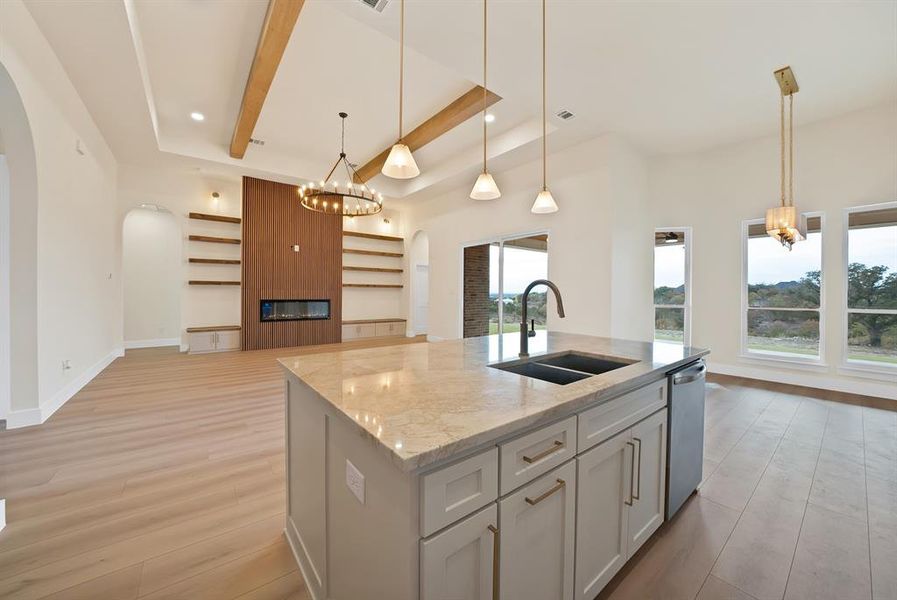 Kitchen with light stone countertops, a kitchen island with sink, arched walkways, light wood-style floors, and open floor plan Kitchen with light stone countertops, a kitchen island with sink, arched walkways, light wood-style floors, and open floor plan