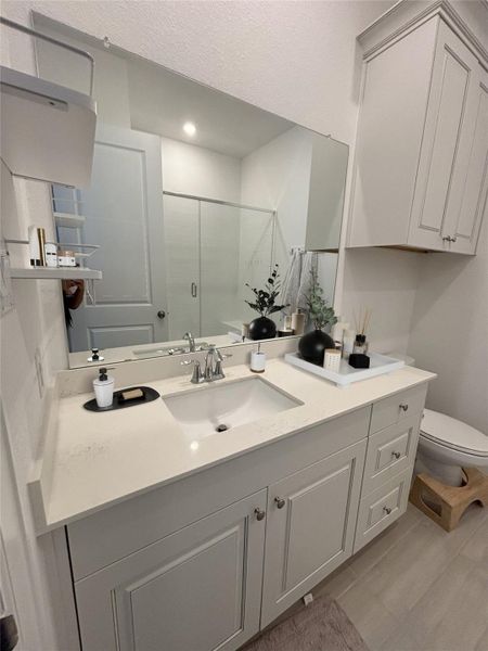 This bathroom features a modern vanity with a sleek countertop and ample storage. It has a large mirror, bright lighting, and a glass-enclosed shower, creating a clean and inviting space.