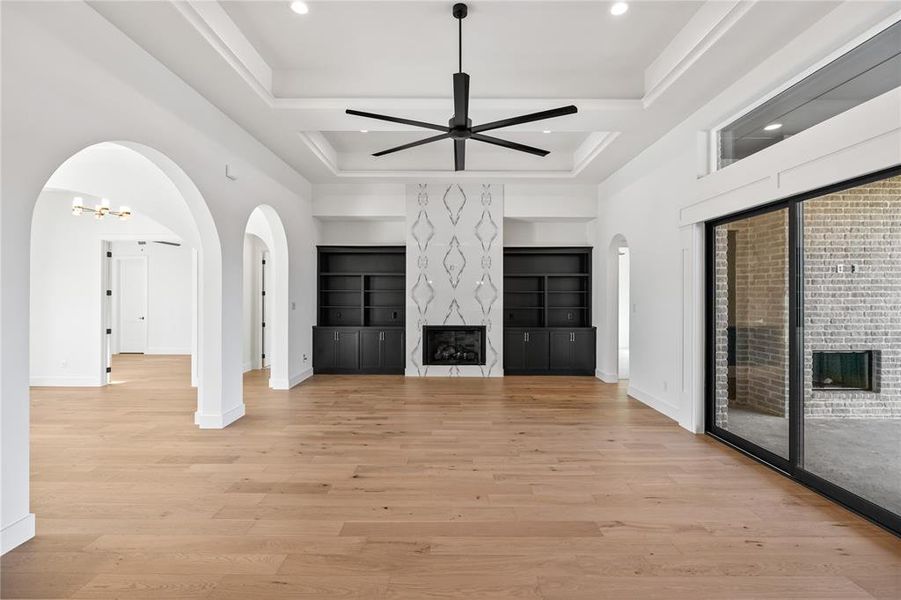 Unfurnished living room with a fireplace, arched walkways, light wood finished floors, ceiling fan, and a tray ceiling Unfurnished living room with a fireplace, arched walkways, light wood finished floors, ceiling fan, and a tray ceiling