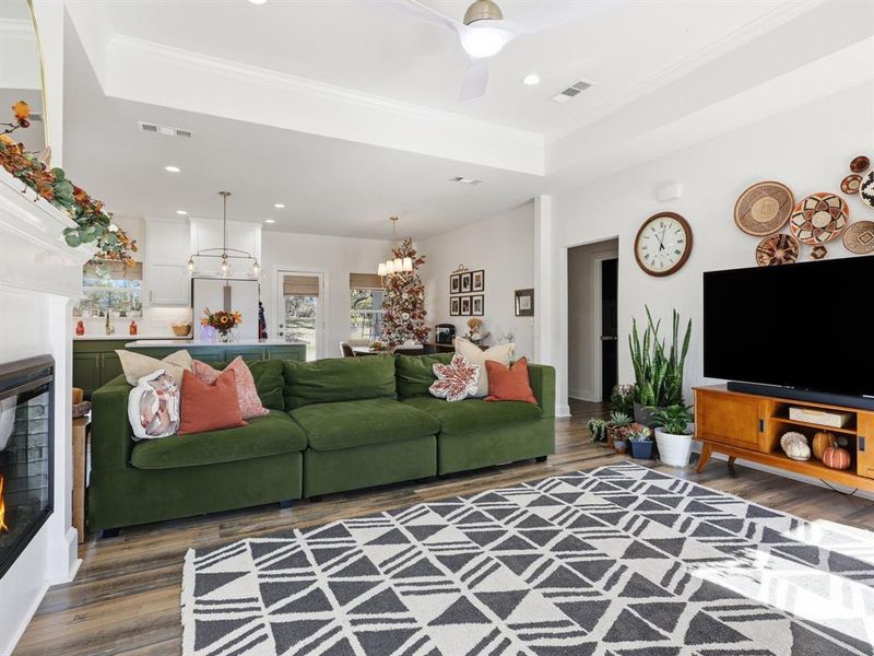Living room featuring a warm lit fireplace, dark wood-style floors, recessed lighting, a ceiling fan, and ornamental molding
