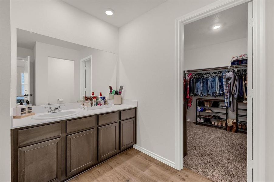 Bathroom featuring vanity, wood finished floors, a walk in closet, baseboards, and recessed lighting