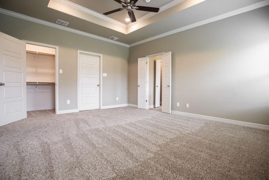 Unfurnished bedroom featuring crown molding, carpet, a tray ceiling, and visible vents
