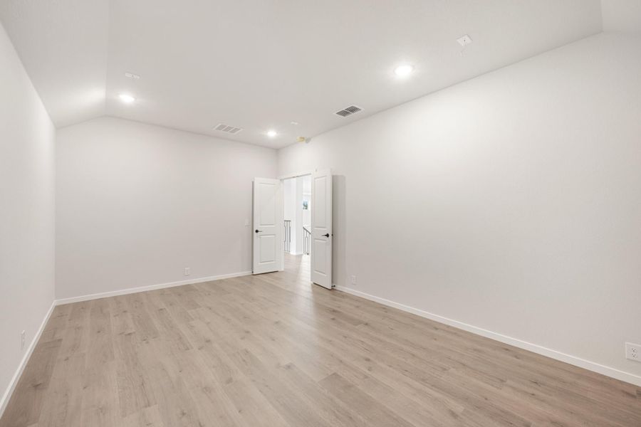 Empty room with light wood floors, white walls, recessed lighting, and double doors opening to hallway Empty room with light wood floors, white walls, recessed lighting, and double doors opening to hallway