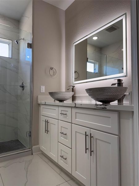 Elegant bathroom featuring a double vanity with vessel sinks, a sleek backlit mirror, and a modern glass-enclosed shower. Elegant bathroom featuring a double vanity with vessel sinks, a sleek backlit mirror, and a modern glass-enclosed shower.