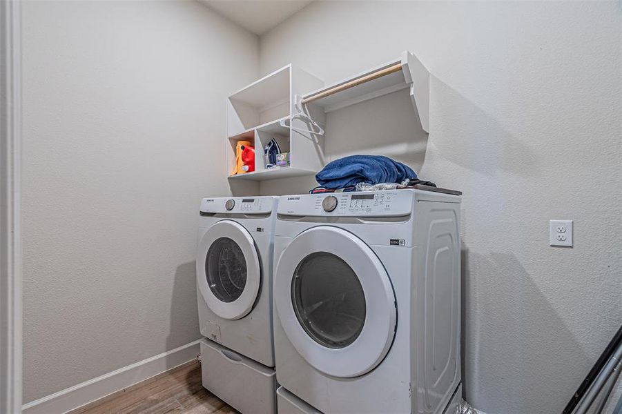 Dedicated laundry area featuring wood-finish flooring, white walls, and built-in white shelving