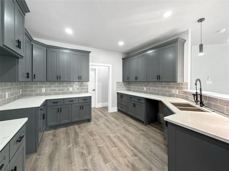 Kitchen with decorative backsplash, gray cabinets, light stone countertops, light wood-type flooring, and pendant lighting