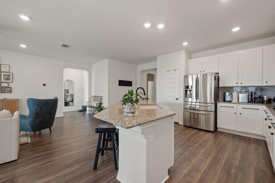 Kitchen with arched walkways, white cabinetry, light stone counters, and recessed lighting