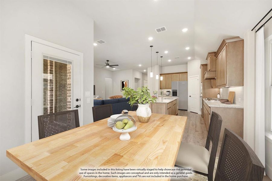 Open-concept dining area with wood table flowing into kitchen with tan cabinets and stainless refrigerator