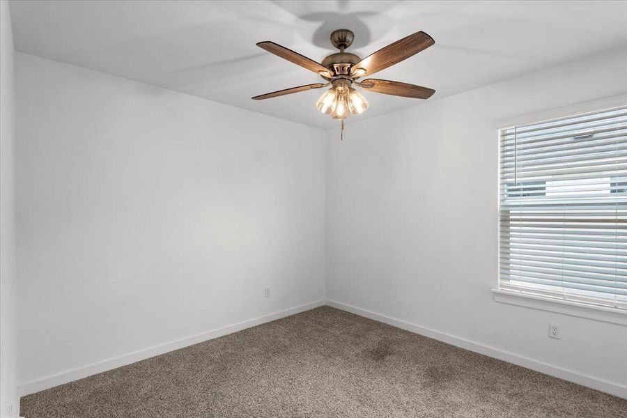 A well-lit bedroom offering a cozy retreat with soft carpeting and a classic ceiling fan.