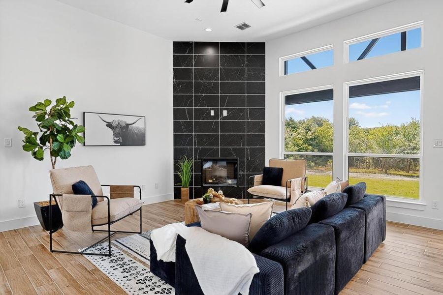 Living room featuring light wood-style floors, a ceiling fan, and a tile fireplace