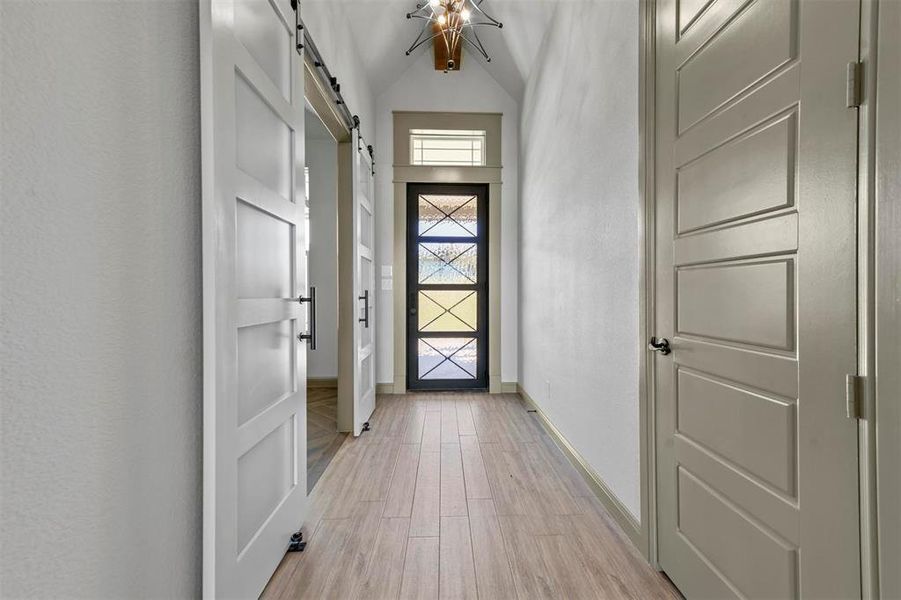 Doorway with a barn door, vaulted ceiling, and light wood-type flooring