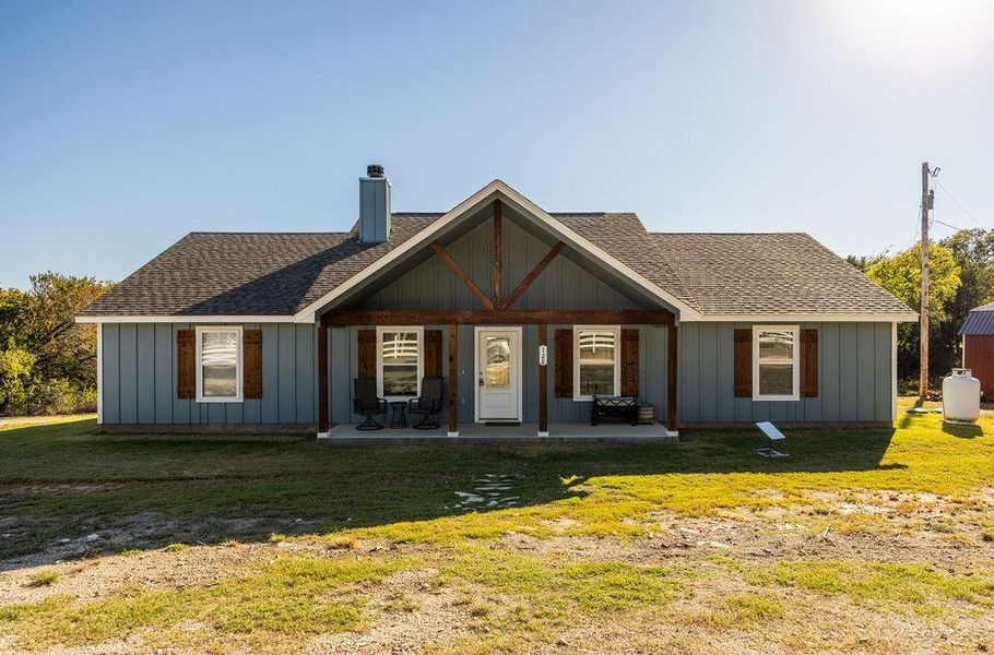 View of front of home with a shingled roof, covered porch, a chimney, and a front lawn