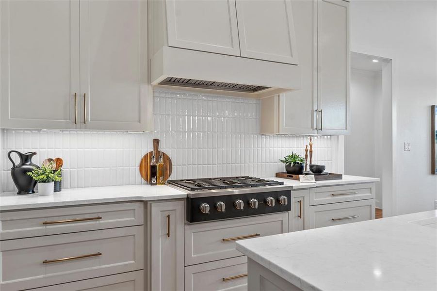 Kitchen featuring custom exhaust hood, stainless steel gas stovetop, decorative backsplash, and light stone counters