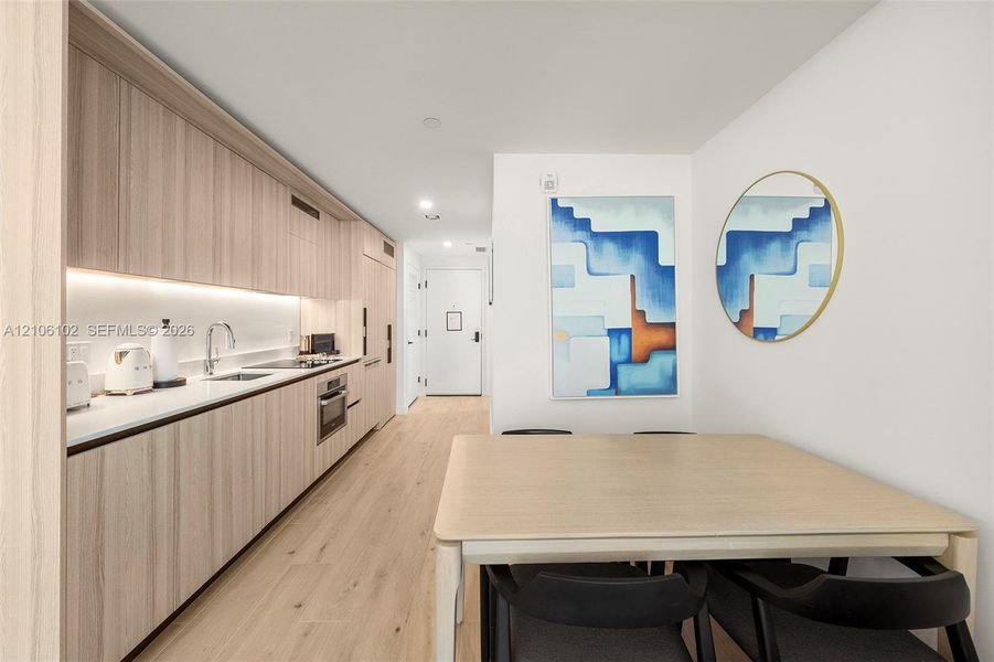 Kitchen featuring light wood-finish cabinetry, solid surface countertops, integrated appliances, under-cabinet lighting, and wood-finish flooring