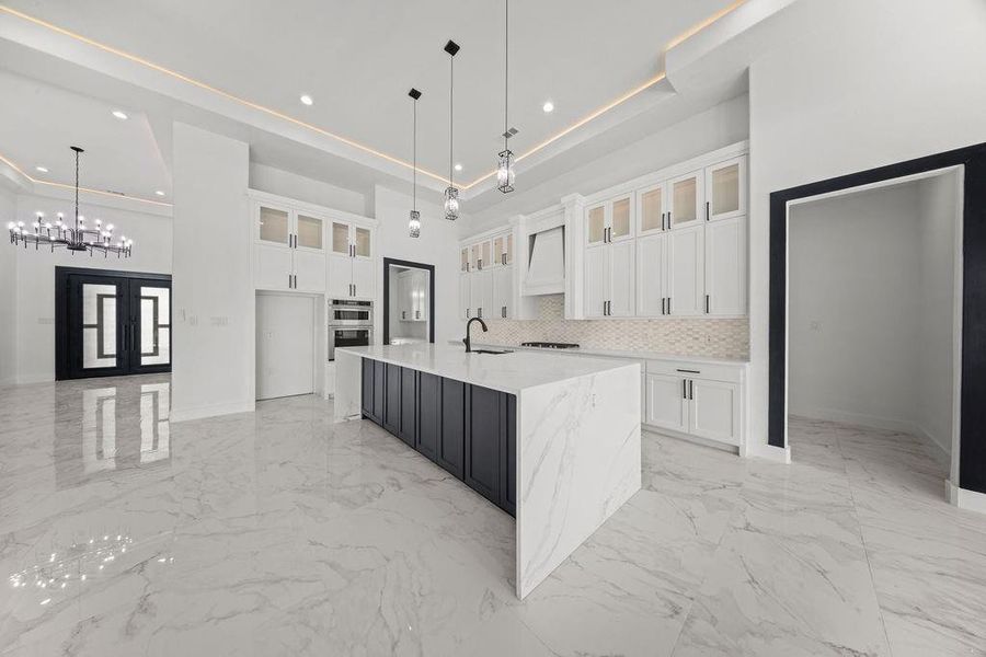 Two tone kitchen with light stone countertops, glass insert cabinets, a spacious island, light marble finish floors, and two tone color scheme