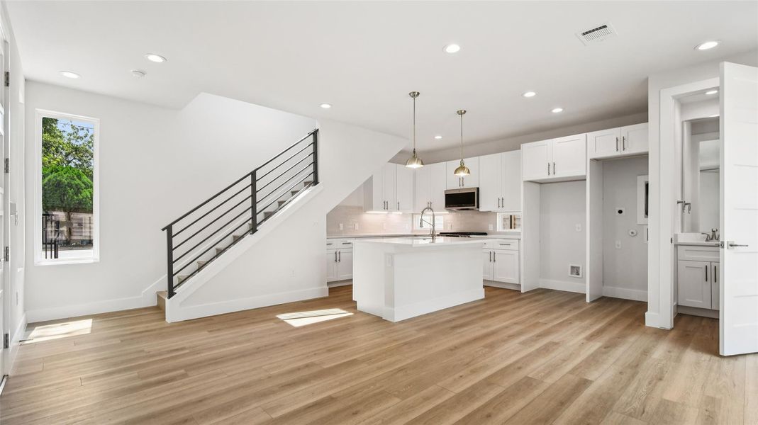 Kitchen with white cabinets, hanging light fixtures, a center island with sink, recessed lighting, and light wood finished floors Kitchen with white cabinets, hanging light fixtures, a center island with sink, recessed lighting, and light wood finished floors