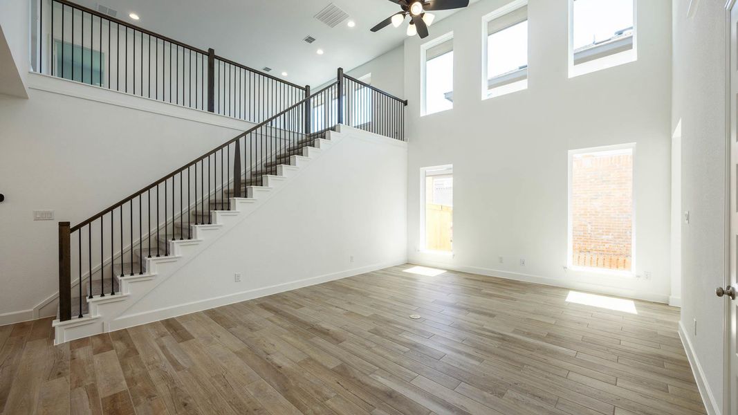 Unfurnished living room with stairway, a high ceiling, light wood-style flooring, and a ceiling fan Unfurnished living room with stairway, a high ceiling, light wood-style flooring, and a ceiling fan