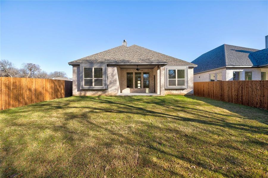 Back of house with ceiling fan and a yard