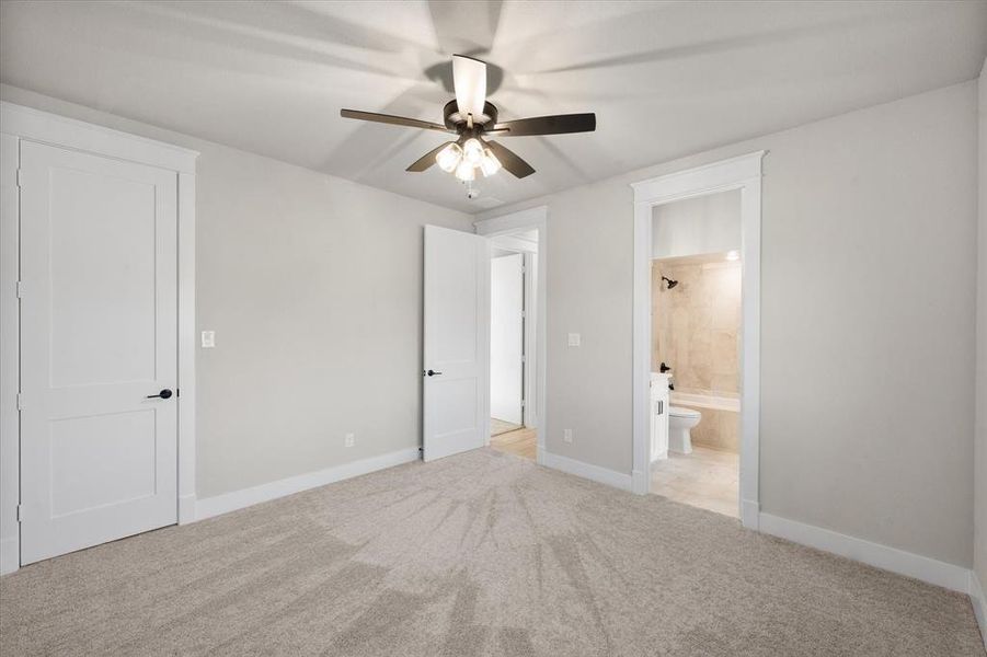 Unfurnished bedroom featuring light carpet, ensuite bathroom, and ceiling fan