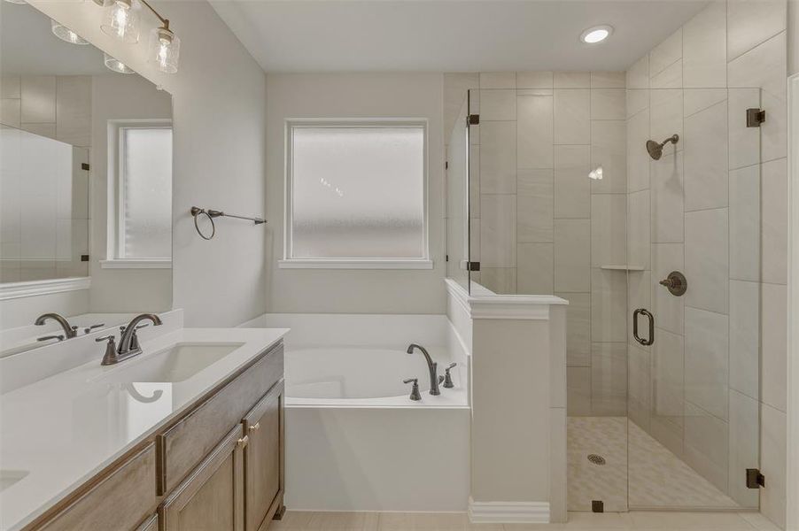 Bathroom featuring a dual-sink vanity with white countertops, a built-in soaking tub, and a glass-enclosed shower with tile surround