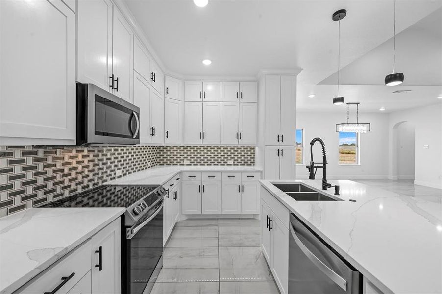 Kitchen with white cabinets, pendant lighting, stainless steel appliances, and decorative backsplash