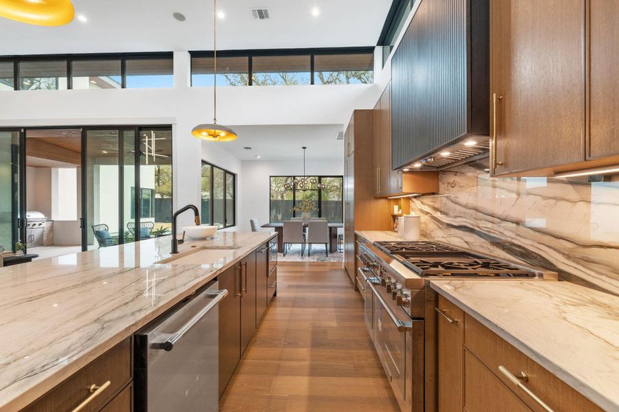 Kitchen with light stone countertops, stainless steel appliances, wood finish cabinetry, and decorative light fixtures