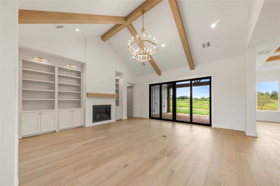 Unfurnished living room with a chandelier, light wood-type flooring, a glass covered fireplace, and plenty of natural light