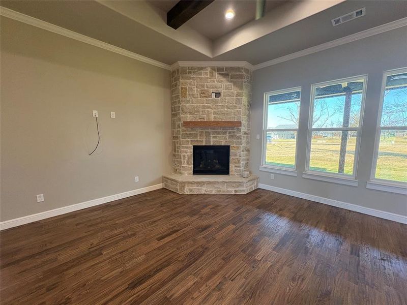Unfurnished living room featuring dark wood-style flooring, a stone fireplace, and ornamental molding
