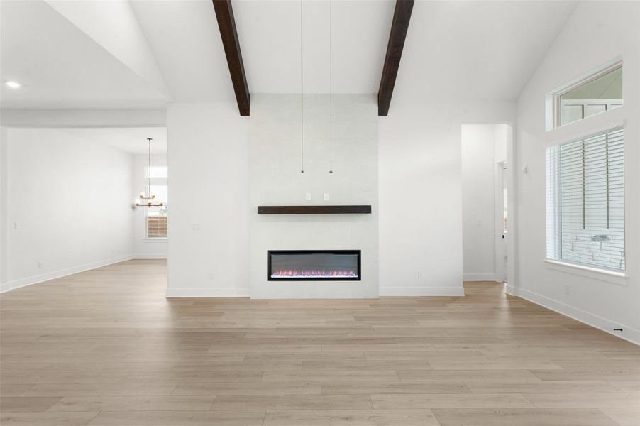 Unfurnished living room featuring a glass covered fireplace, beam ceiling, light wood-type flooring, high vaulted ceiling, and a chandelier