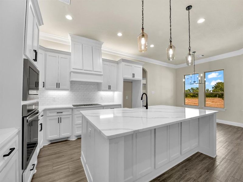 Kitchen with white cabinets, light stone countertops, a kitchen island with sink, and black stovetop