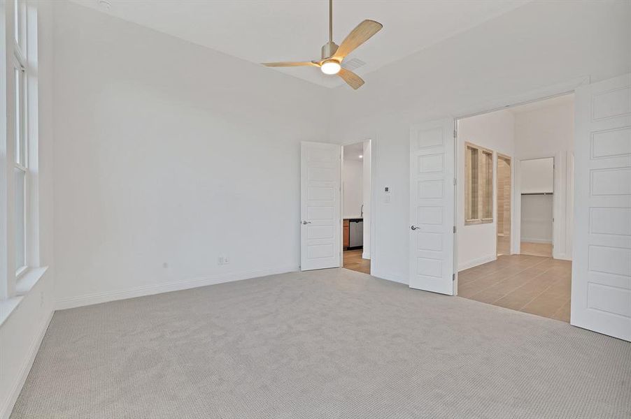 Primary bedroom with ceiling fan, light colored carpet, ensuite bathroom, and vaulted ceiling