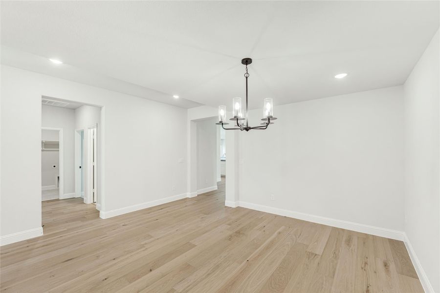 Empty dining room with light wood floors, white walls, and a black chandelier
