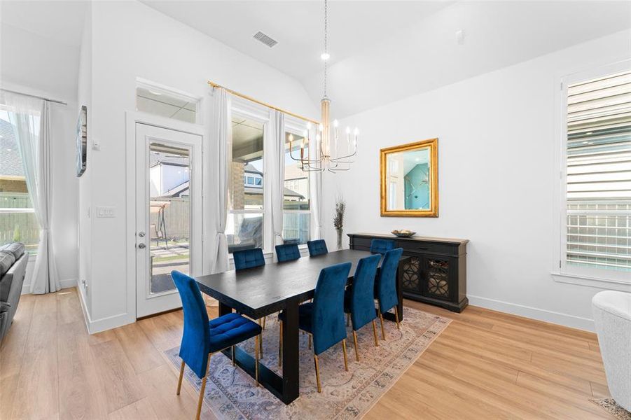 Dining area featuring light wood flooring, white walls, and a contemporary chandelier