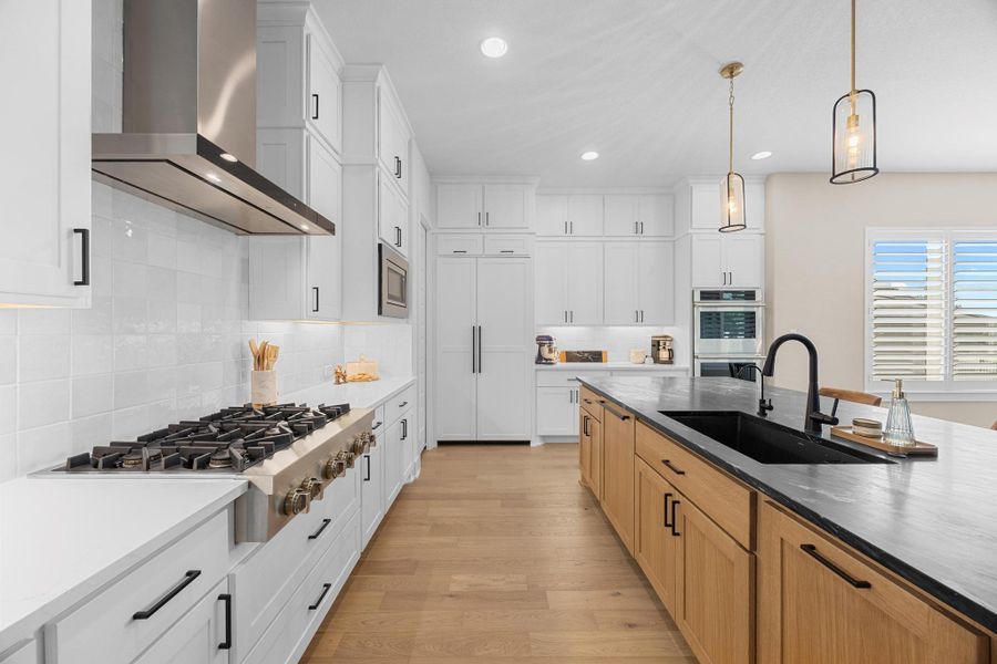 Kitchen featuring light wood finished floors, wall chimney exhaust hood, stainless steel appliances, recessed lighting, and hanging light fixtures