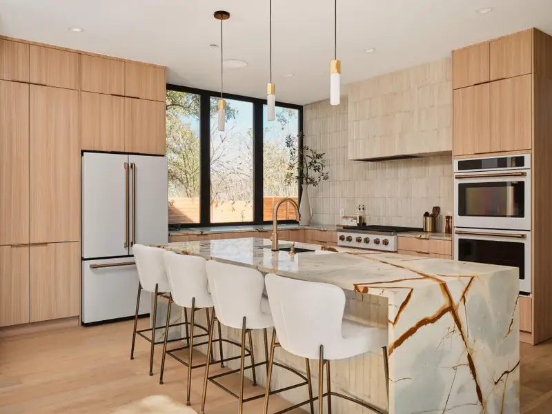 Kitchen featuring light wood finish cabinetry, decorative light fixtures, white appliances, light stone countertops, and modern cabinets
