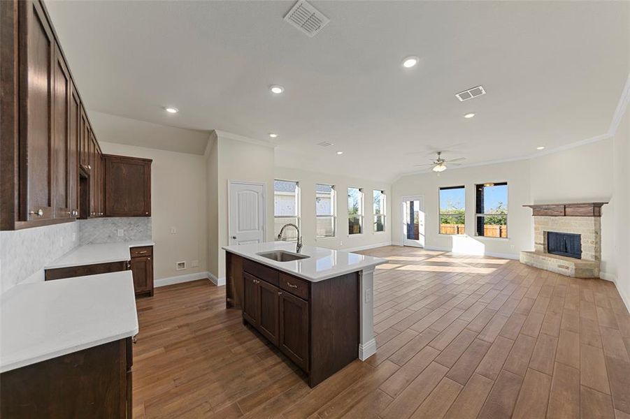 Kitchen with a kitchen island with sink, ceiling fan, sink, wood-type flooring, and a fireplace