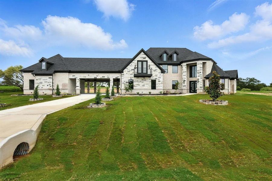 French country home with driveway, a front yard, stone siding, and brick siding