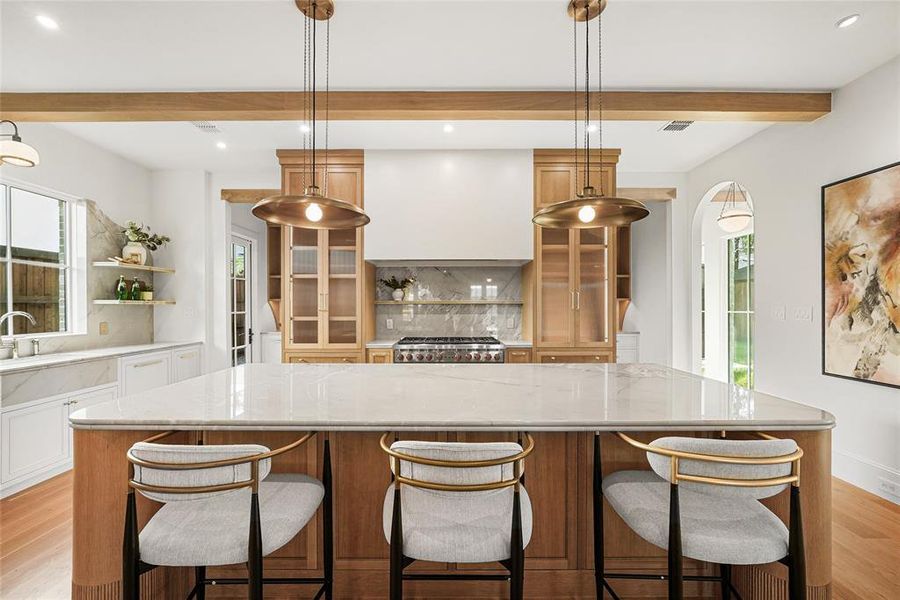 Gourmet kitchen with a substantial central island, light wood-finish cabinetry, built-in range, and two brass-finish pendant lights