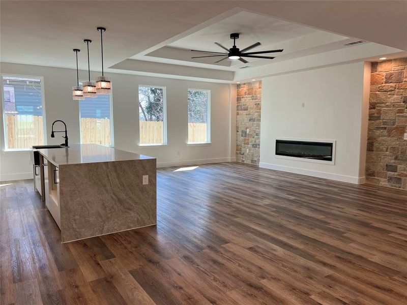 Unfurnished living room with a raised ceiling, dark wood-type flooring, ceiling fan, and a glass covered fireplace