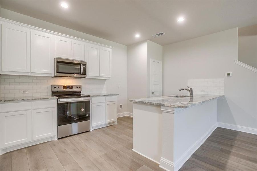 Kitchen featuring tasteful backsplash, appliances with stainless steel finishes, light stone counters, light wood-type flooring, and a peninsula Kitchen featuring tasteful backsplash, appliances with stainless steel finishes, light stone counters, light wood-type flooring, and a peninsula