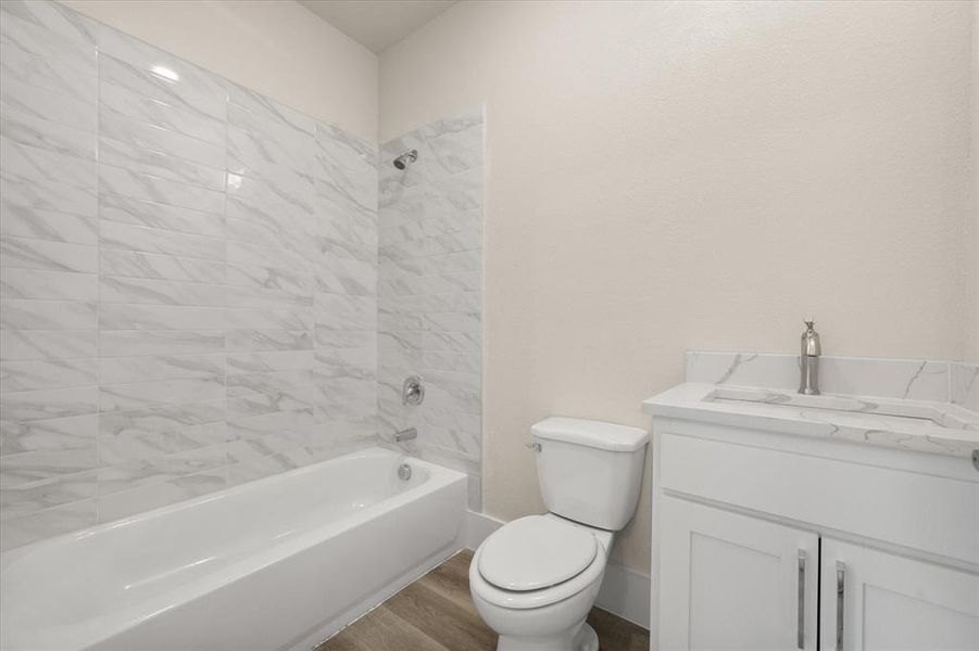 Full bathroom with wood-type flooring, toilet, vanity, and tiled shower / bath combo