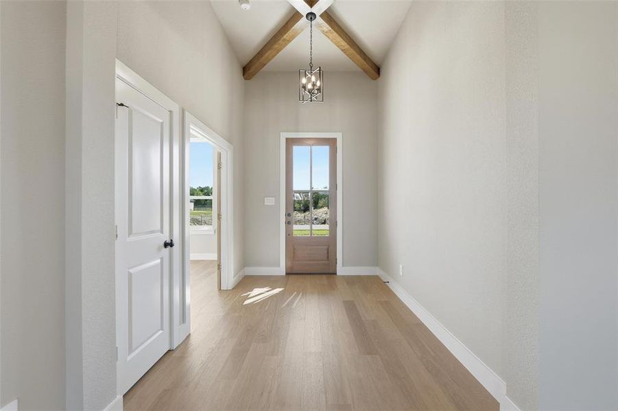 Doorway to outside featuring beamed ceiling, wood finished floors, a chandelier, and a high ceiling