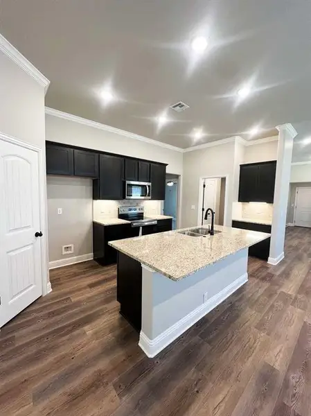 Kitchen with an island with sink, stainless steel appliances, dark cabinets, a sink, and crown molding