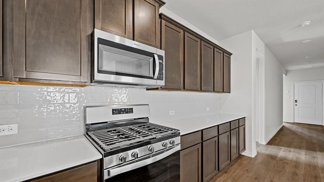 Kitchen featuring stainless steel appliances, dark wood-finish cabinetry, light countertops, and a white subway tile backsplash Kitchen featuring stainless steel appliances, dark wood-finish cabinetry, light countertops, and a white subway tile backsplash